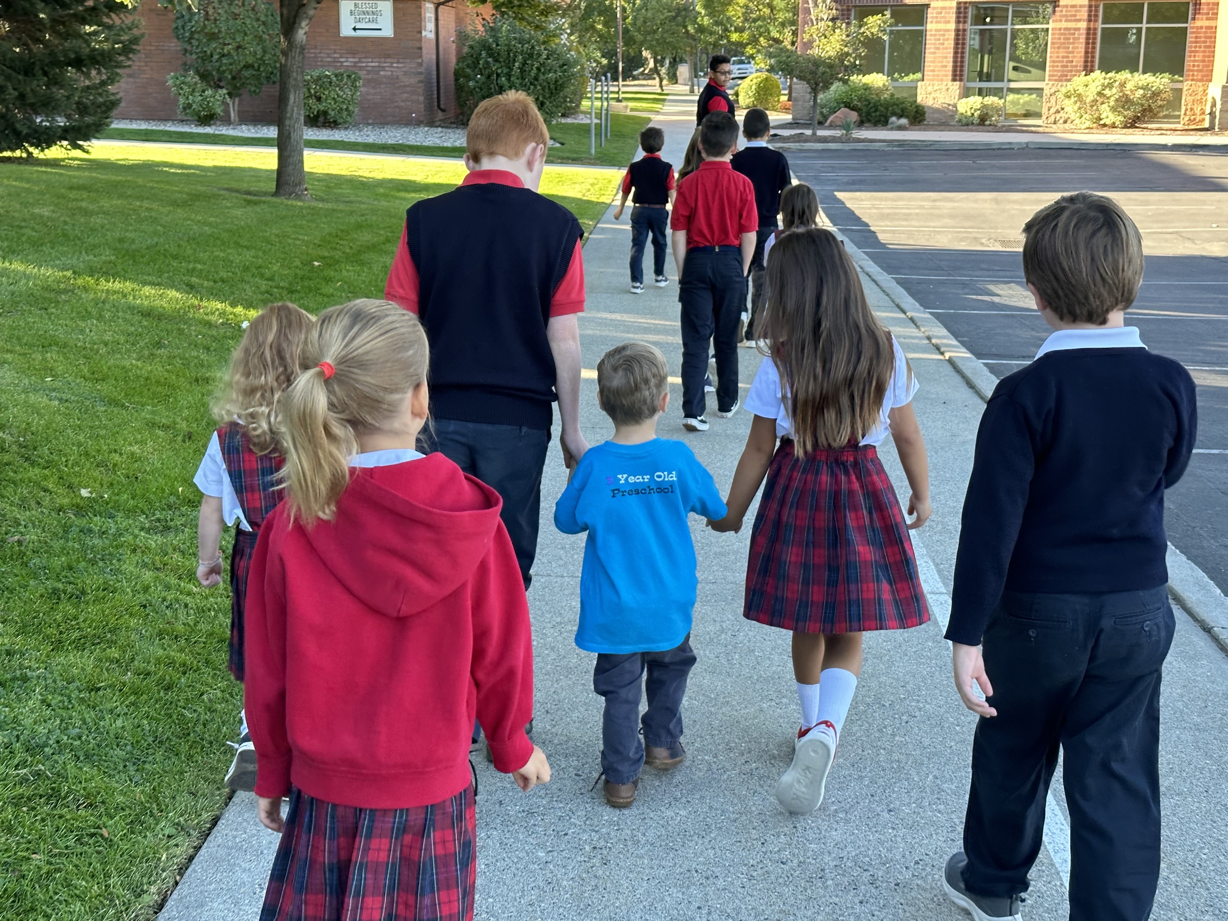 two older children holding the hands of a small child as they walk to mass