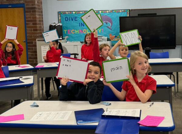 students holding up with boards with the correct answer written on them in French.
